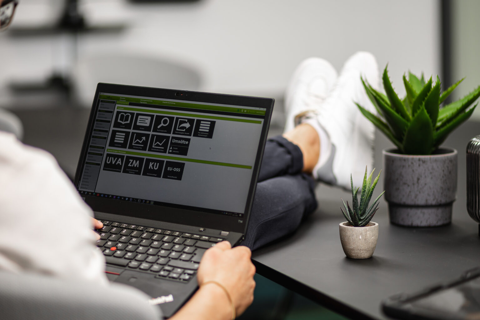 Person sitzt bei einem Bürotisch, hat lässig die Füße am Tisch und die Buchhaltung für GmbHs am Laptop geöffnet.