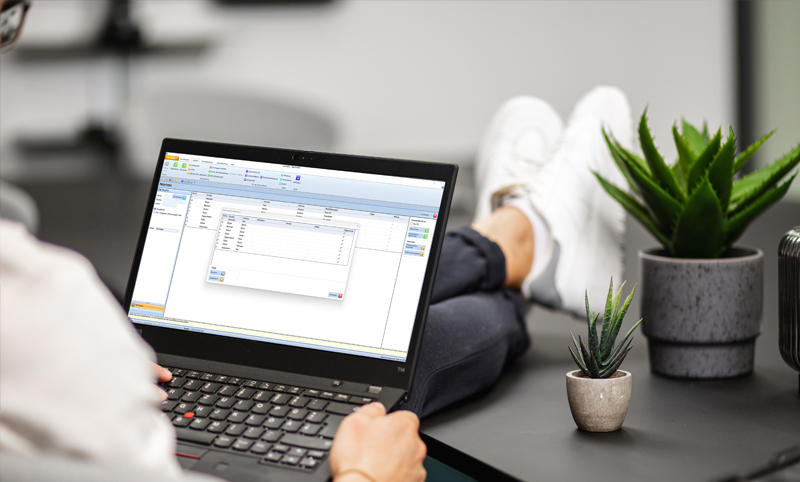 Person sitzt bei einem Bürotisch, hat lässig die Füße am Tisch und die Lohnverrechnungssoftware für Vereine am Laptop geöffnet.